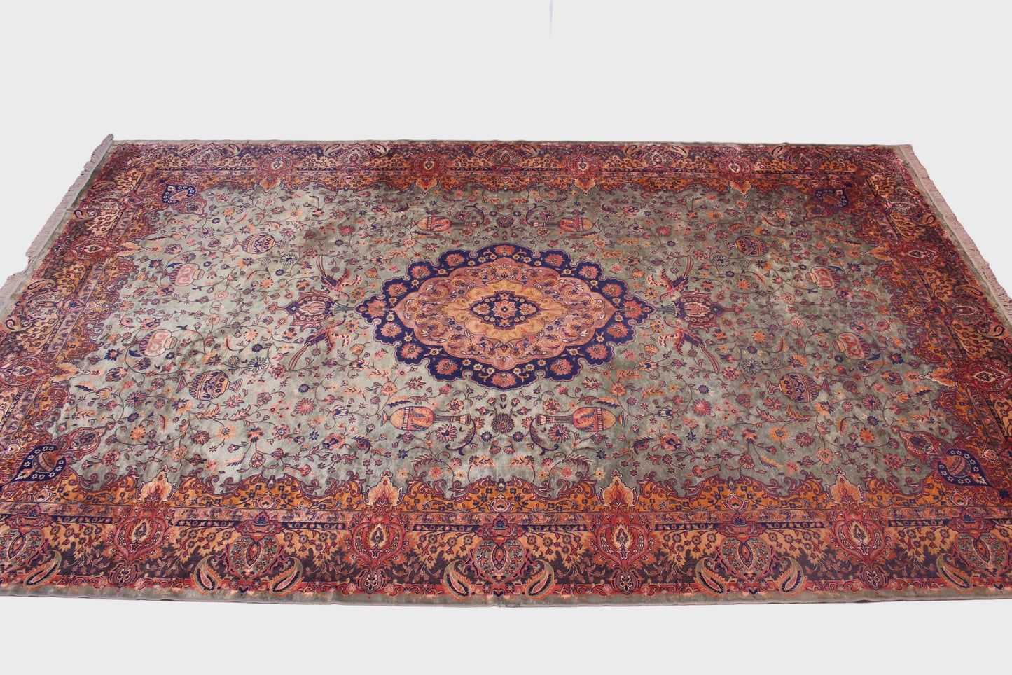 A large traditional oriental area rug with an intricate floral and medallion pattern, displayed on a brown tiled floor in an indoor showroom setting.