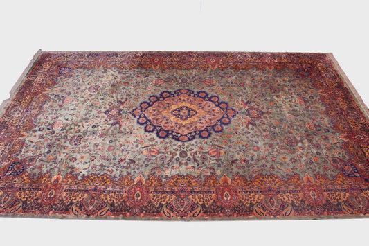 A large traditional oriental area rug with an intricate floral and medallion pattern, displayed on a brown tiled floor in an indoor showroom setting.